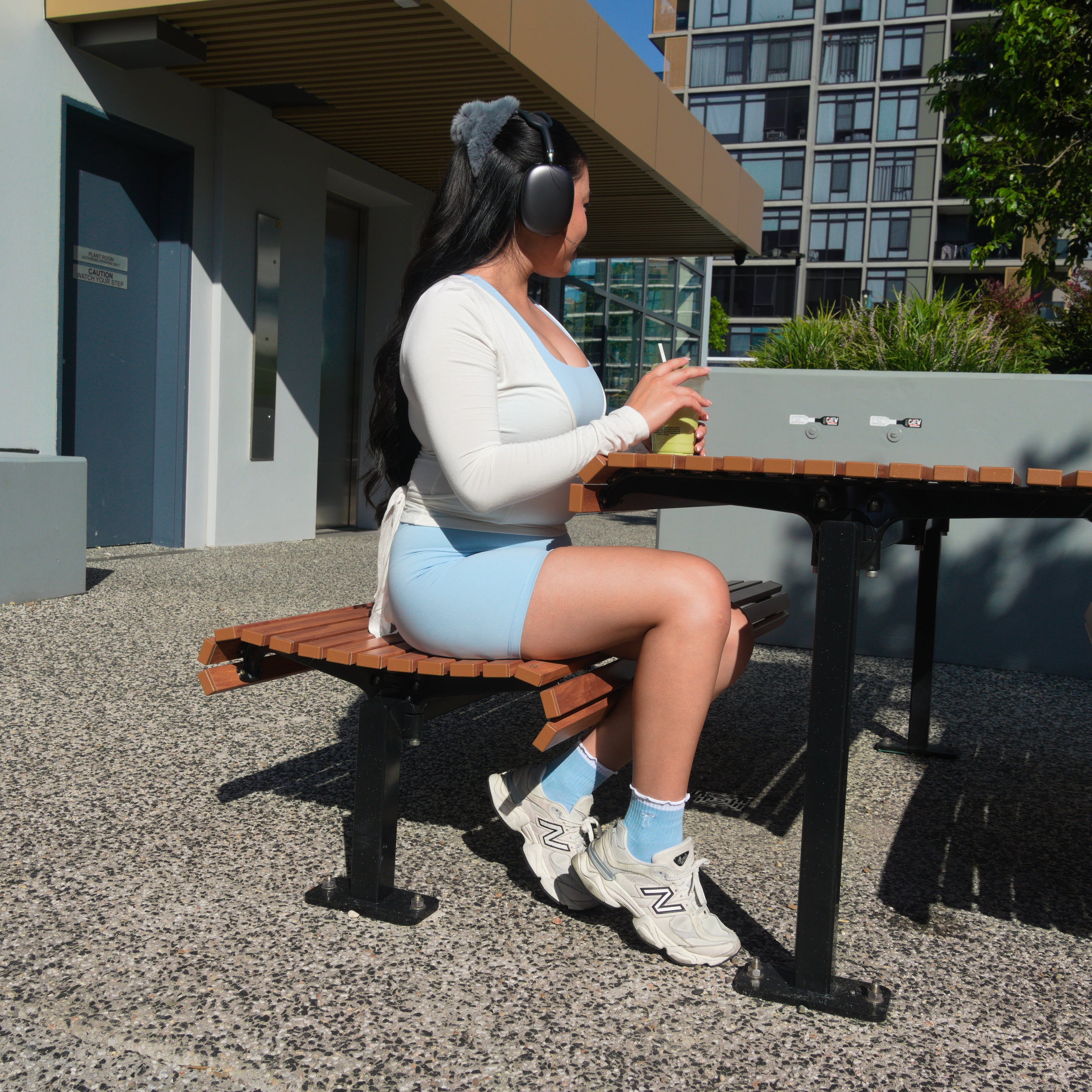 Person sitting on a bench at an outdoor table with buildings and trees in the background