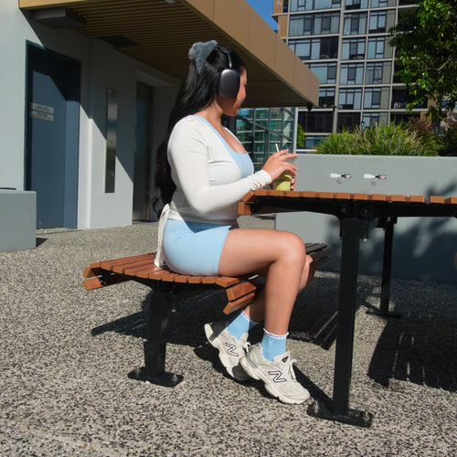 Person sitting on a bench at an outdoor table with buildings and trees in the background