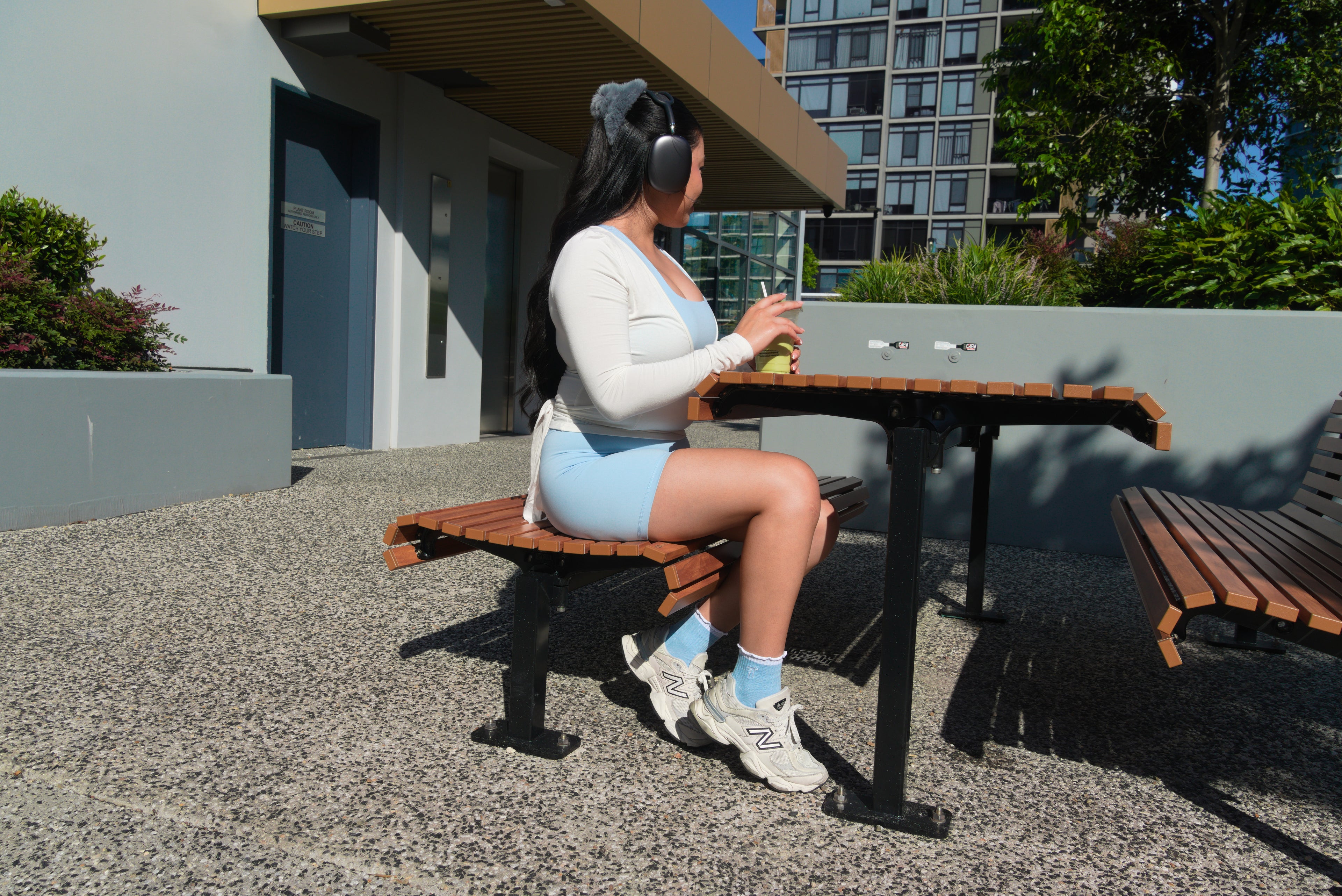 Person sitting on a bench at an outdoor table with buildings and trees in the background