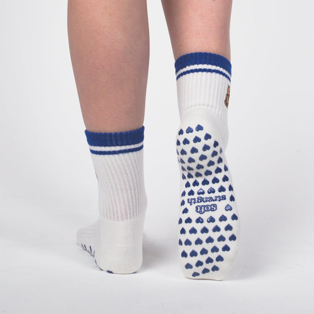 A person shown from the waist down wearing black athletic shorts with a white drawstring, white crew socks with blue stripes, and white socks with blue triangle grip dots on the sole, standing against a light gray studio background.