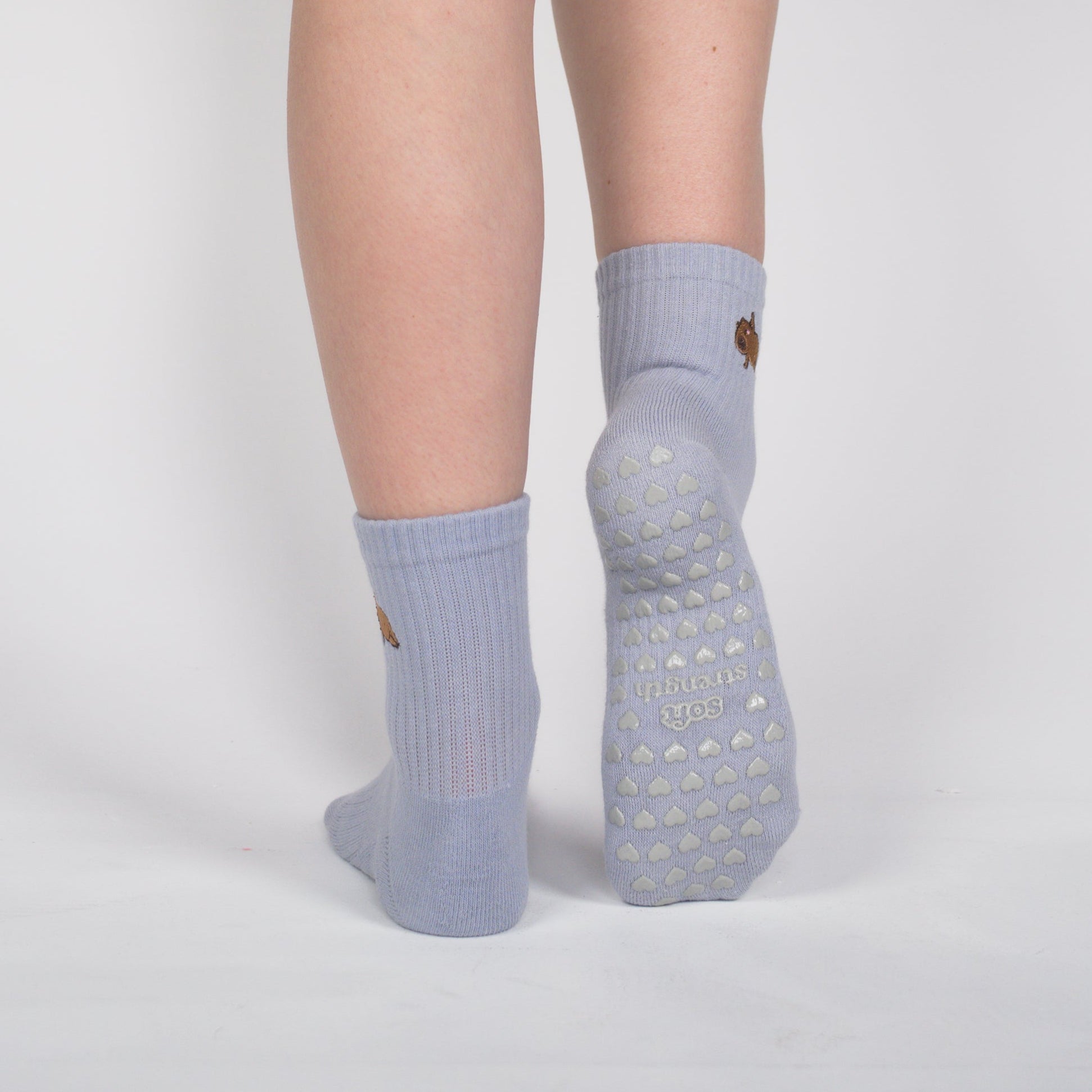 A person shown from the back wearing black biker shorts and light blue grip socks with textured soles, standing against a light gray studio background.
