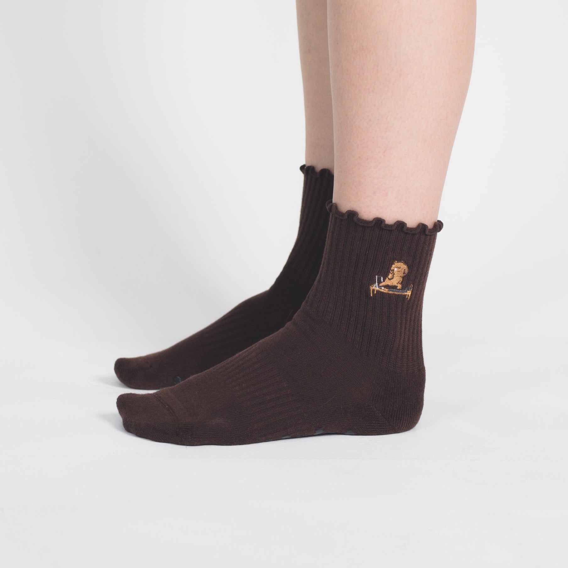 A pair of dark brown ankle socks worn on a person's feet, shown against a plain light gray studio background.