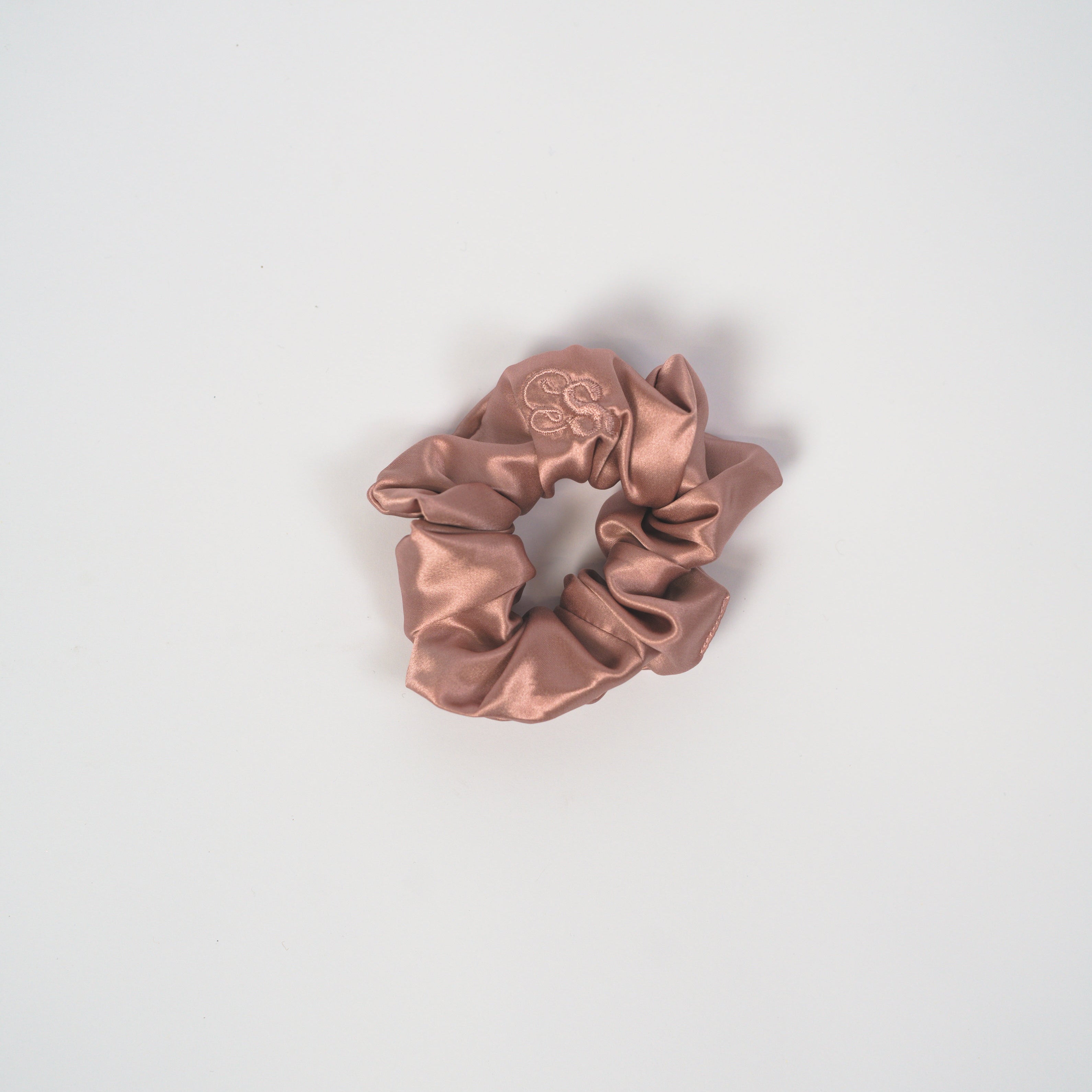 A single satin scrunchie in a dusty rose or mauve color, centered on a clean, light gray background.
