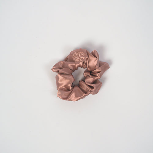 A single satin scrunchie in a dusty rose or mauve color, centered on a clean, light gray background.