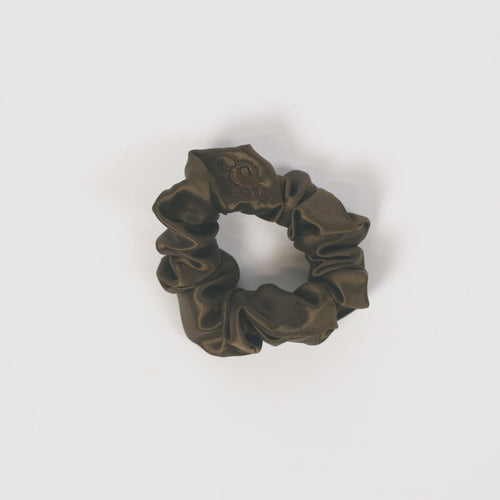 A dark olive green fabric scrunchie with a subtle camouflage pattern, centered on a plain white background.