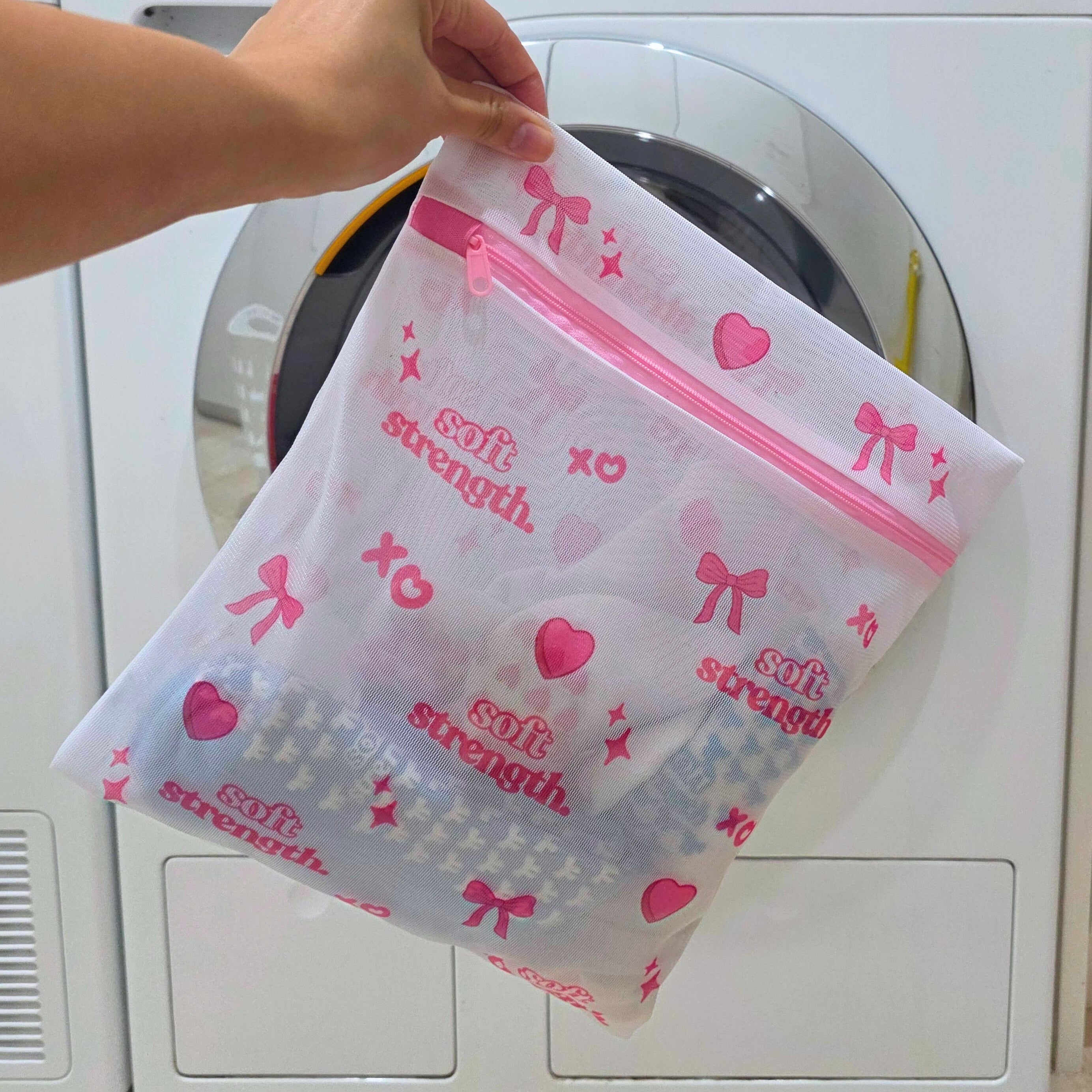 Person holding a mesh laundry bag with pink accents in front of a washing machine.